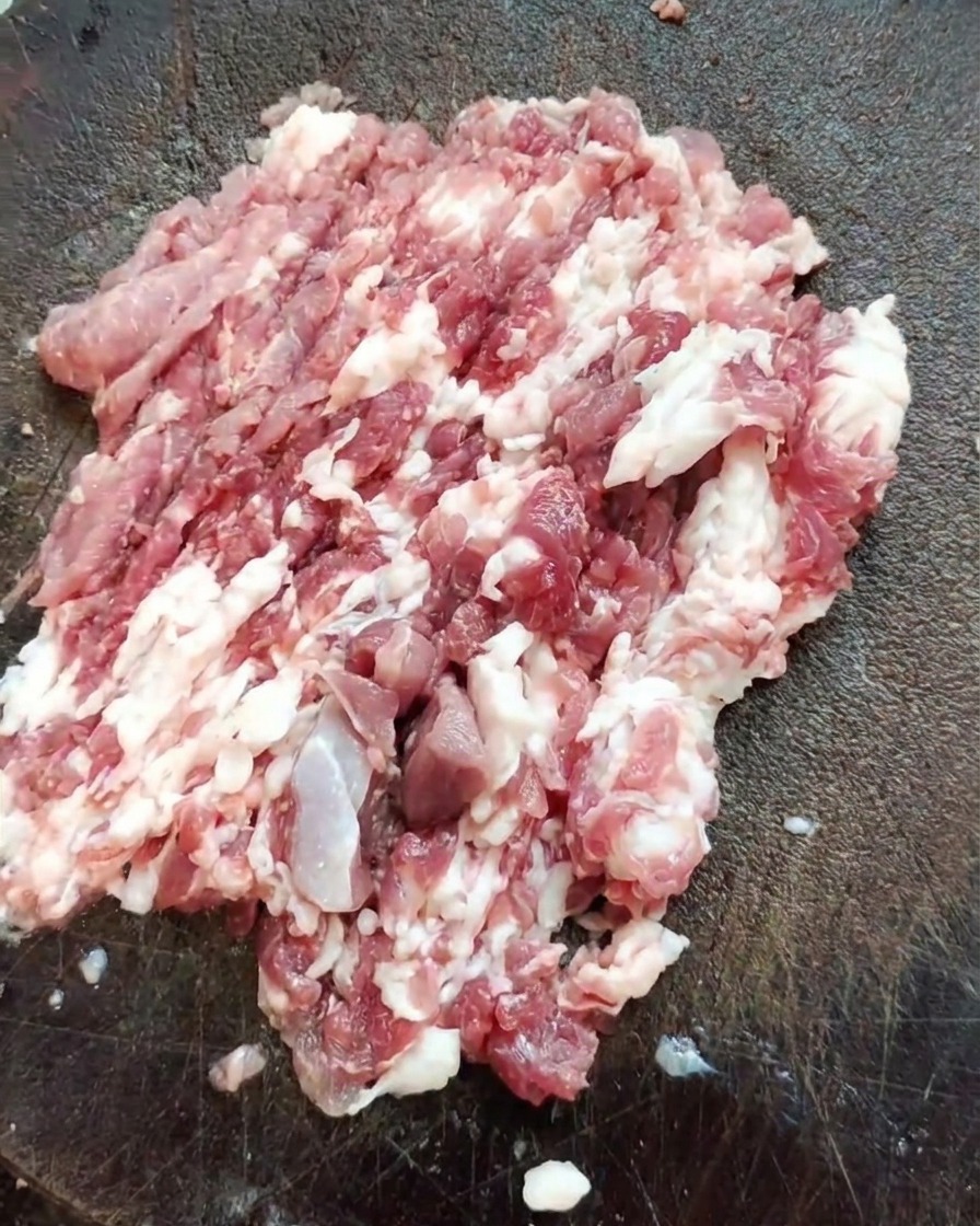 Una mannaia affilata appoggiata su un mucchio di spalla di maiale fresca tritata su un tagliere in legno testurizzato.