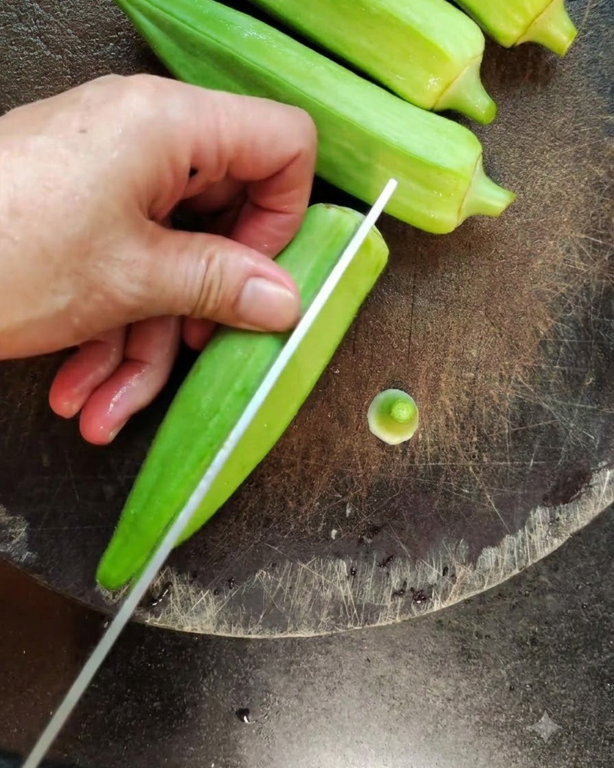Un primo piano di un coltello che taglia a metà per il lungo unokra verde fresca su un tagliere scuro.