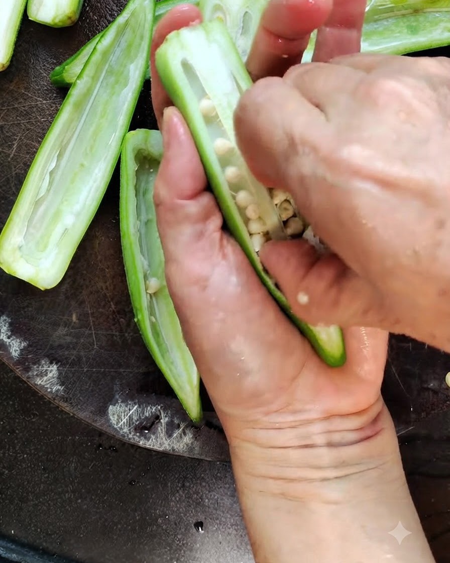 Un coltello da cucina che taglia a metà esattamente per il lungo un baccello di okra verde fresco su un tagliere di legno.