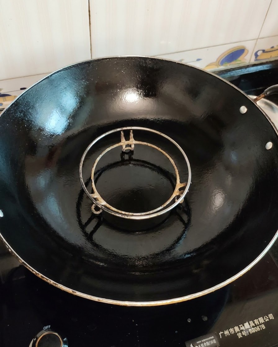 Un cestello per la cottura al vapore vuoto inserito allinterno di un grande wok nero pronto per la cottura.