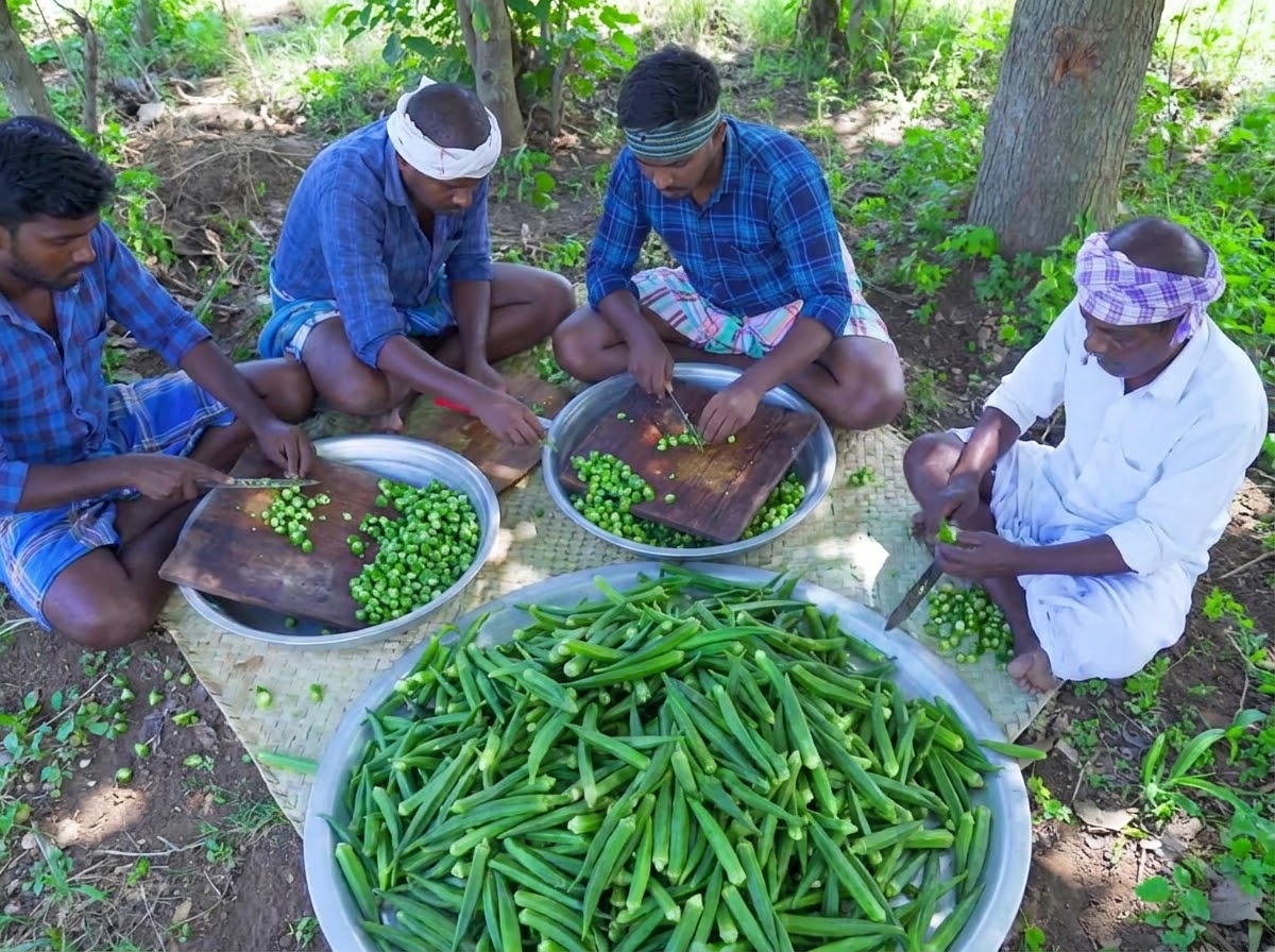 Diverse persone sedute che tagliano okra verde cruda su taglieri di legno.
