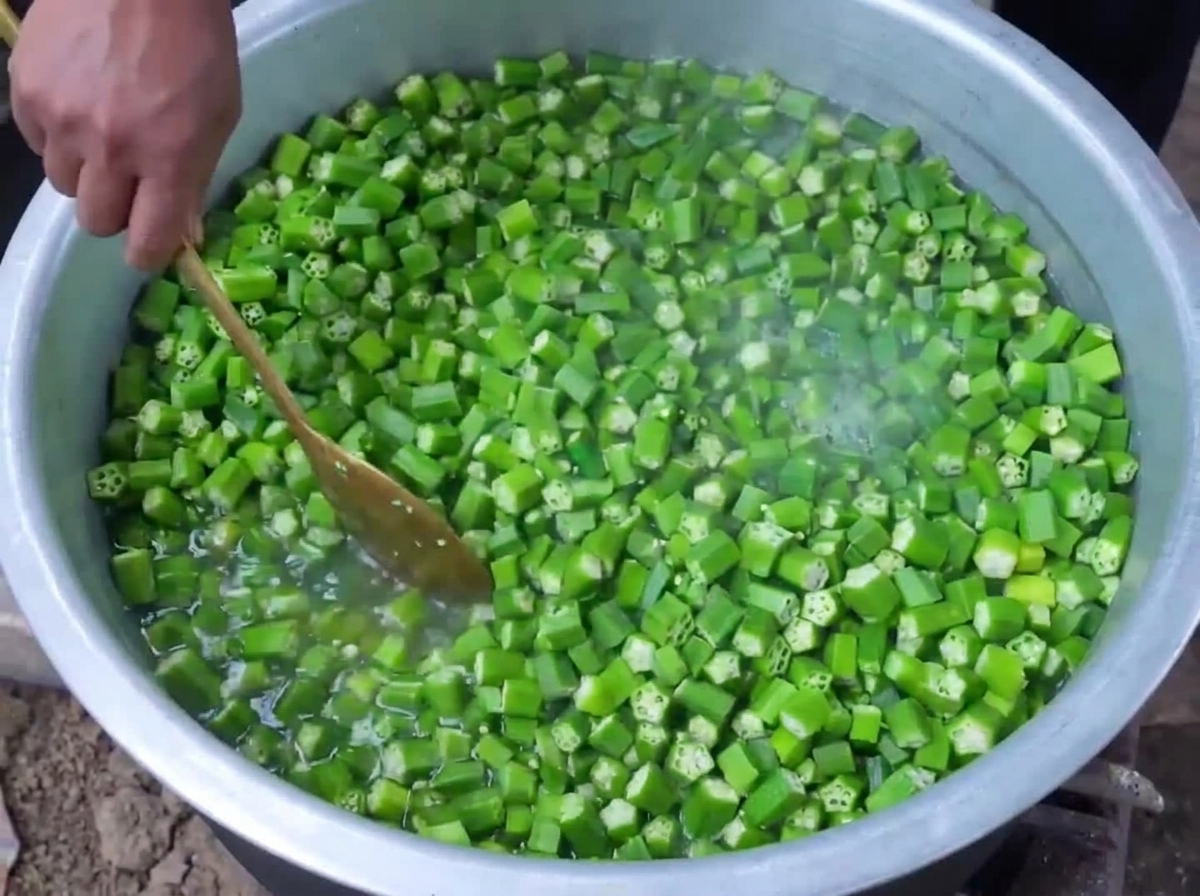 Okra verde tagliata che viene sbollentata in acqua bollente allinterno di una grande pentola mentre viene mescolata con un cucchiaio di legno.