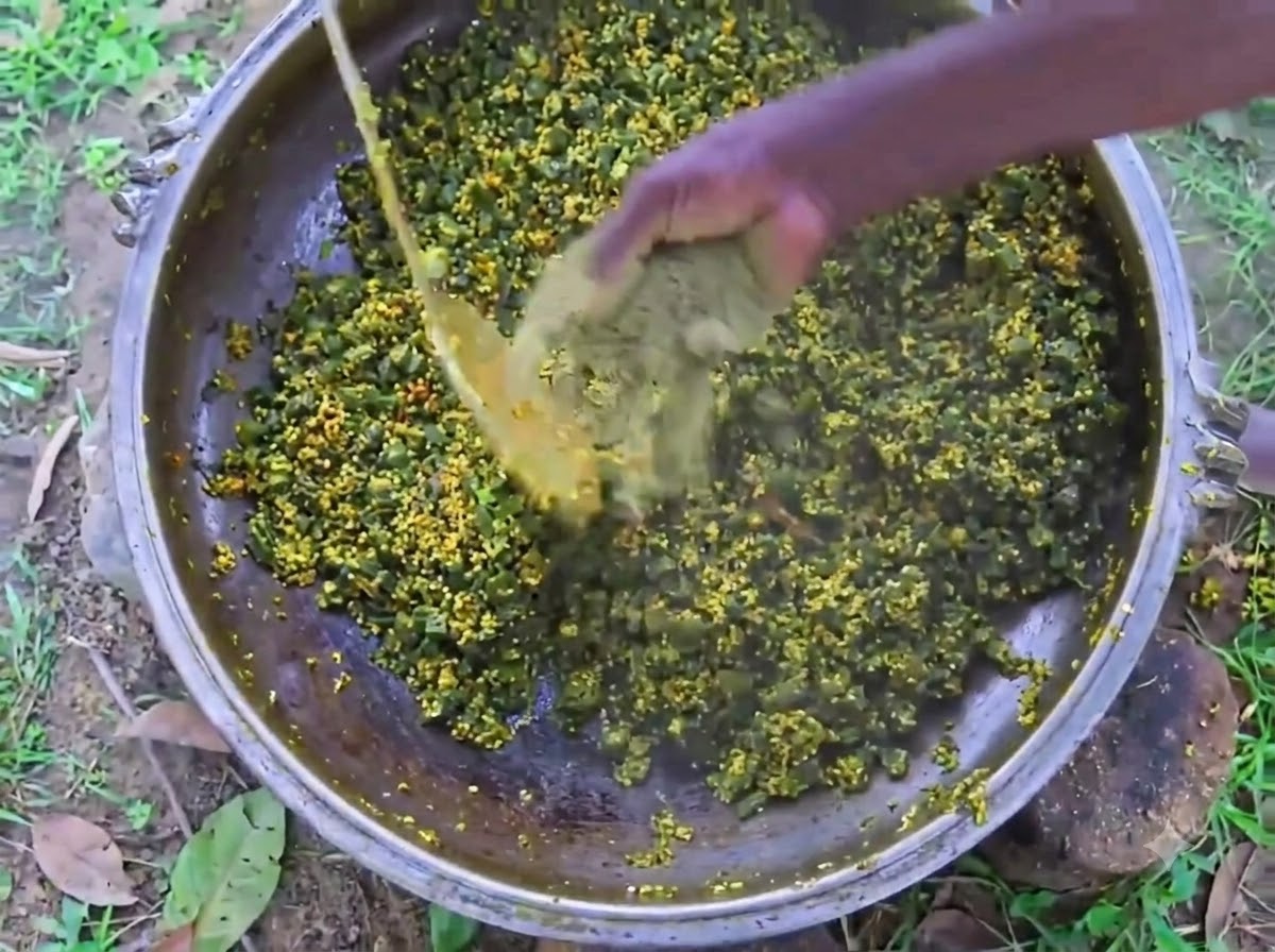 La mano di una persona che mescola pepe nero in polvere in una grande pentola di ferro riempita di okra e uova in cottura.