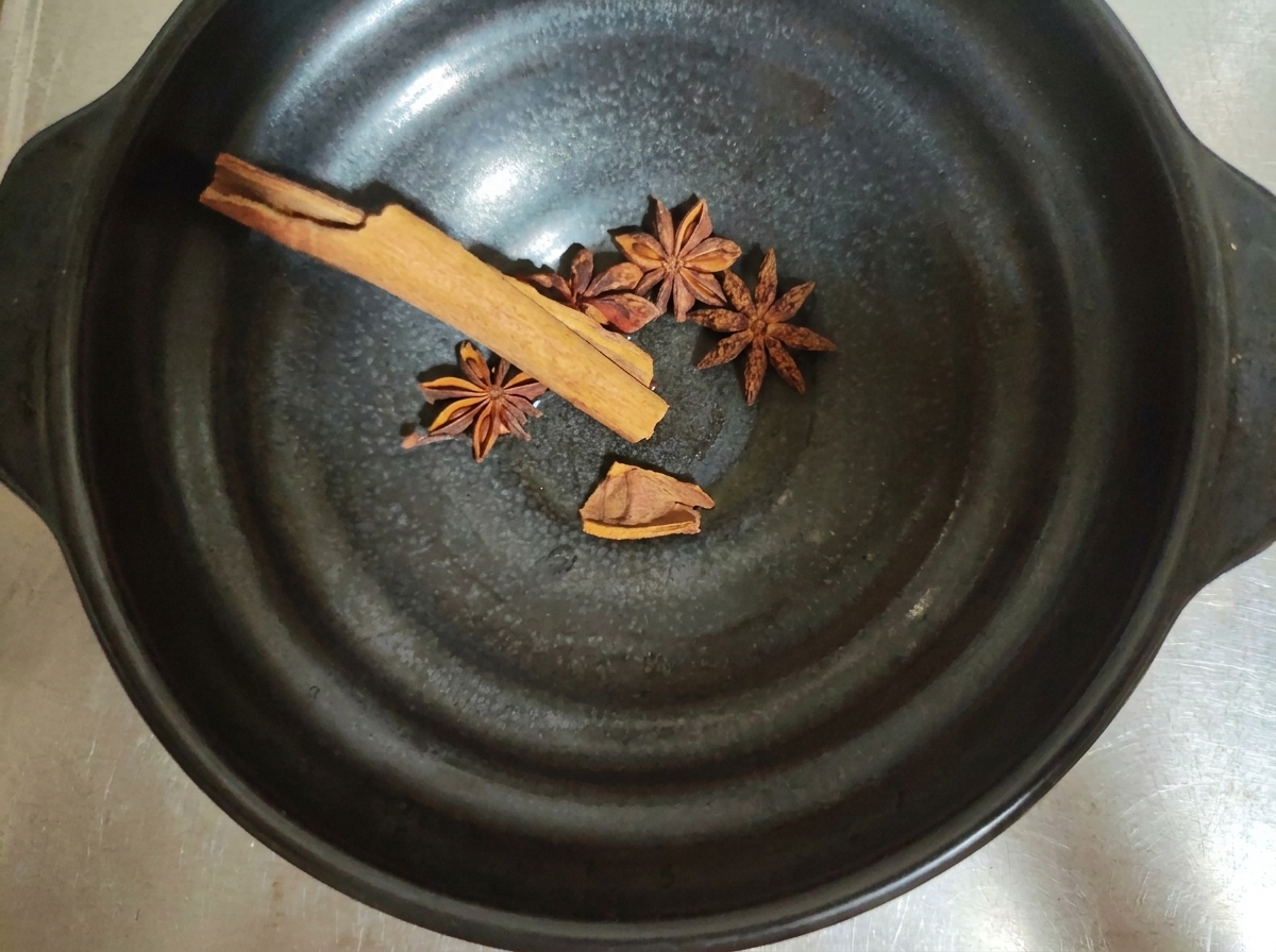 Spezie intere come anice stellato e stecche di cannella dentro una ciotola scura.