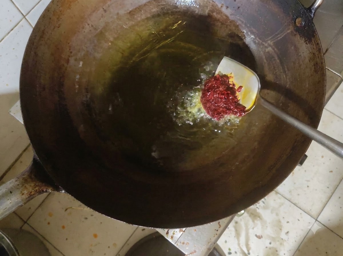Pasta doubanjiang mescolata nellolio caldo allinterno di un wok.