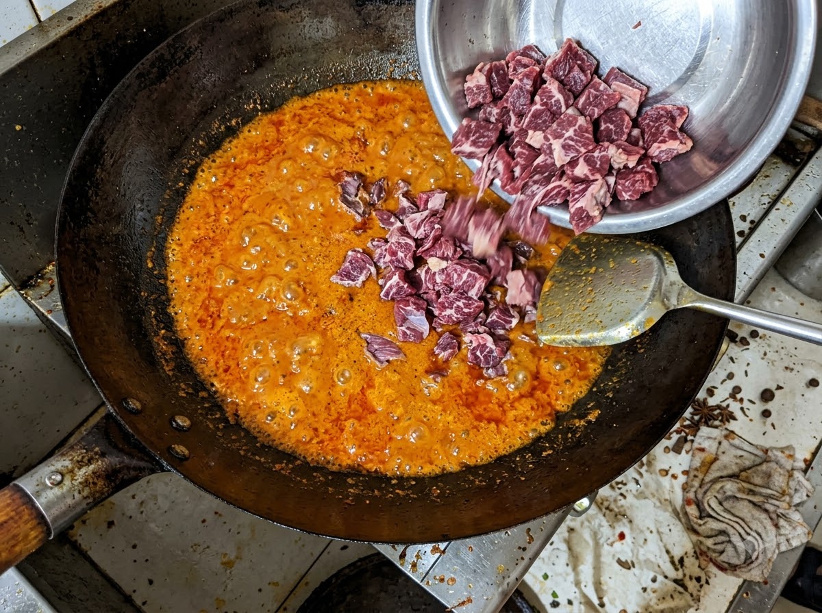 Bocconcini di punta di petto di manzo versati da una ciotola di metallo in un composto di olio di peperoncino rosso ribollente in un wok.