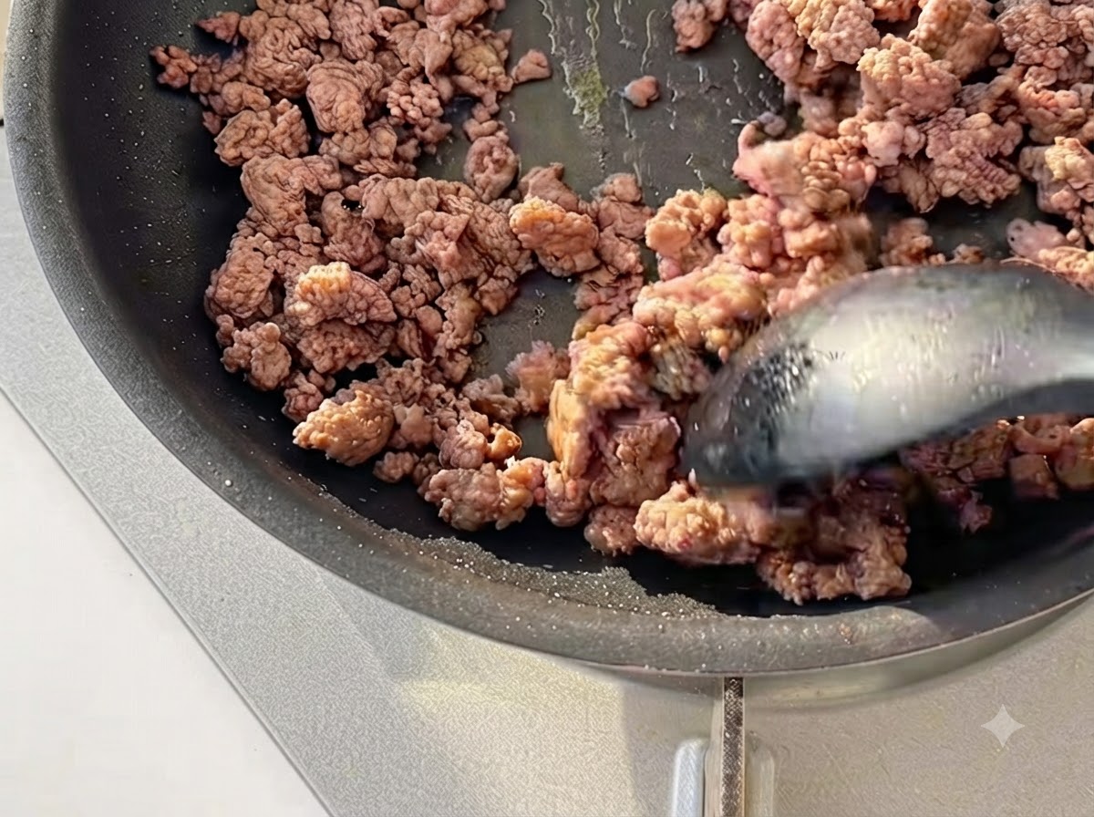 Carne macinata saltata con una spatola in una padella nera fino a doratura leggera.