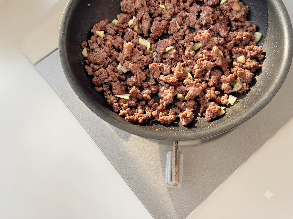 Aglio tritato e pomodori a cubetti saltati insieme alla carne macinata dorata in una padella.