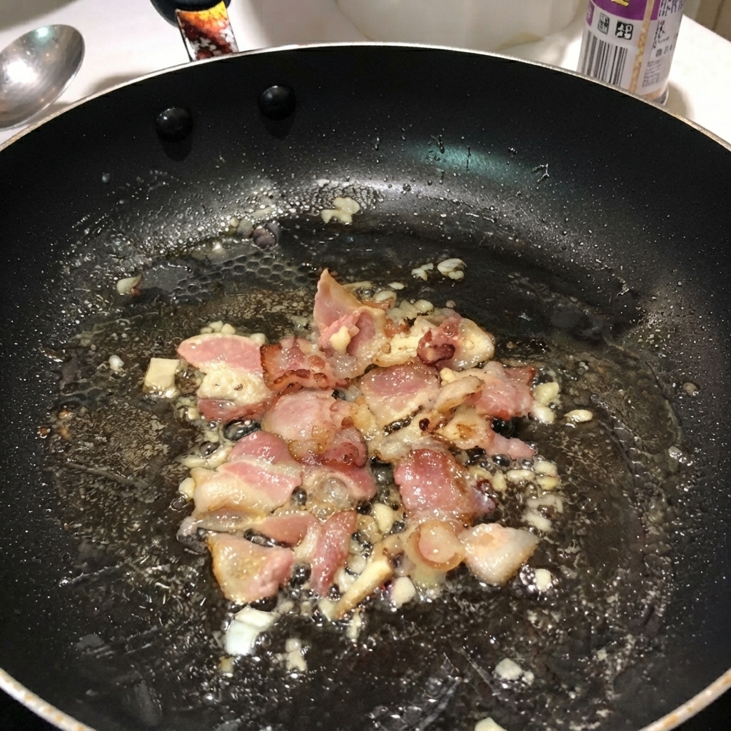 Pasta penne bollita mescolata con bacon e cipolle allinterno di una padella nera.