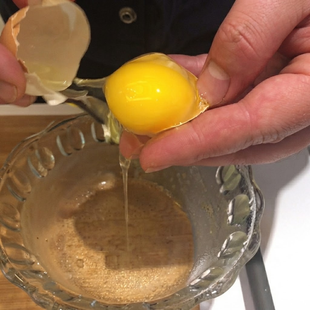 Un tuorlo duovo aperto e fatto cadere dal suo guscio in una ciotola di vetro trasparente.