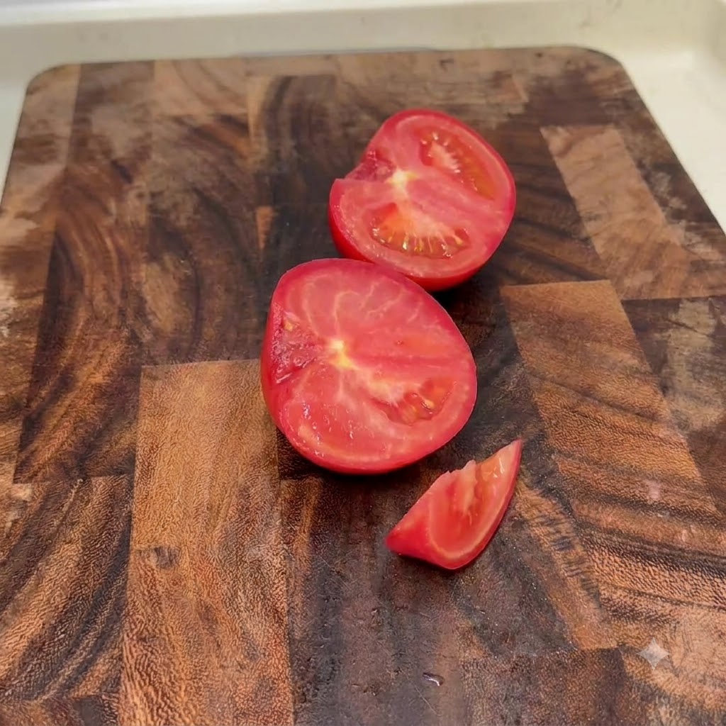 Pomodori freschi tagliati a metà e a piccoli pezzi su un tagliere di legno.