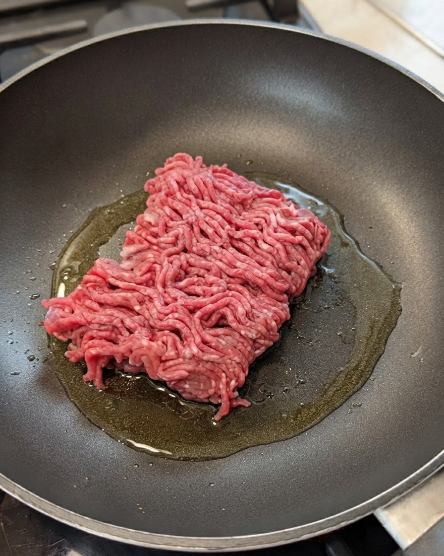 Carne macinata cruda in una padella con olio, cipolle e aglio.