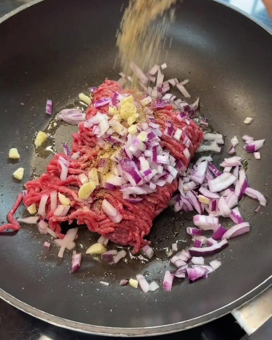 Spezie versate sopra la carne macinata e le cipolle in una padella.