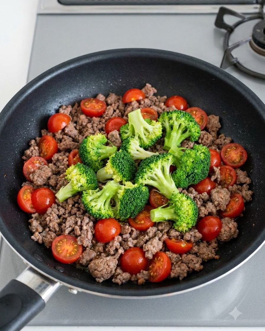 Cimette di broccoli verdi e pomodorini rossi brillanti sparsi sulla carne macinata cotta in padella.