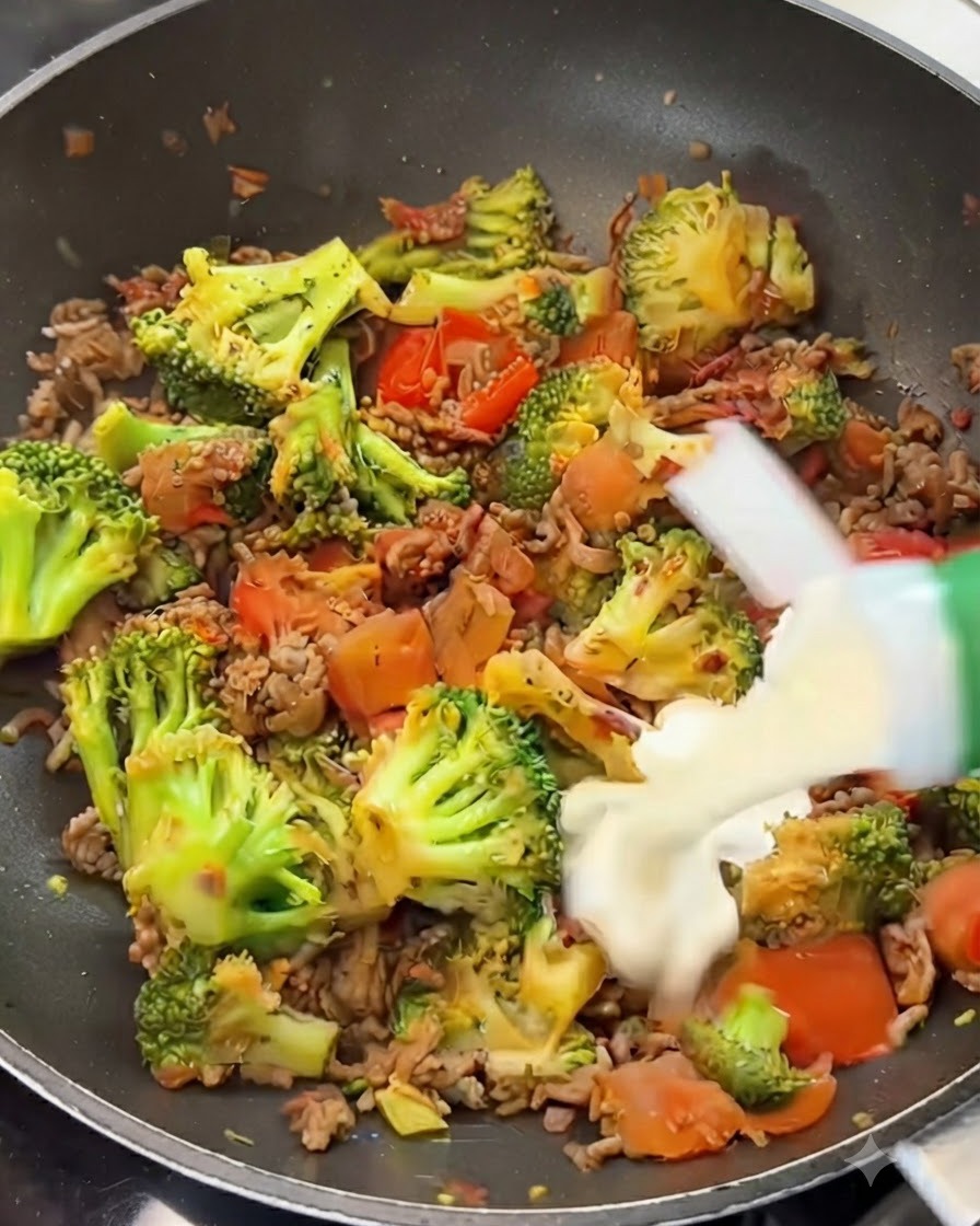 Panna da cucina versata da un cartone su un miscuglio di manzo, broccoli e pomodori in padella.