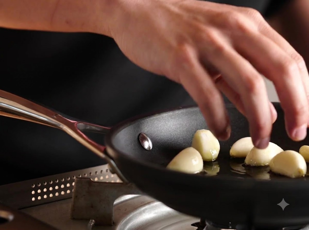 Spicchi daglio interi pelati fatti cadere in una padella con olio doliva.