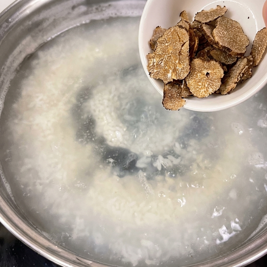 Delle fette di tartufo vengono versate da una piccola ciotola bianca in una pentola di acqua in ebollizione.