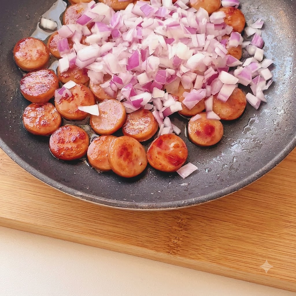 Cipolla rossa tritata finemente sparsa sui pezzi di salsiccia dorati in padella.
