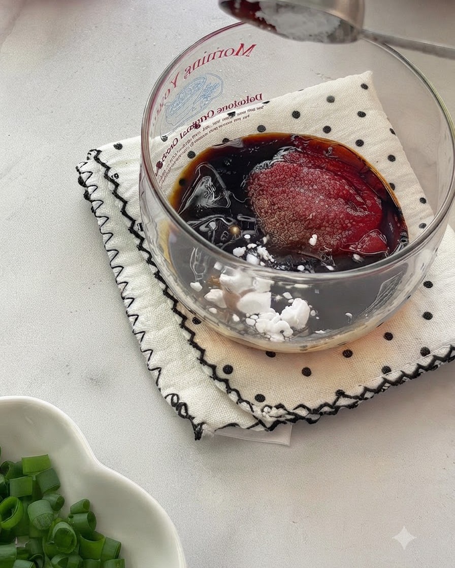 Un cucchiaio che mescola una salsa liquida omogenea allinterno di una ciotola di vetro posta su una superficie di stoffa fantasia.