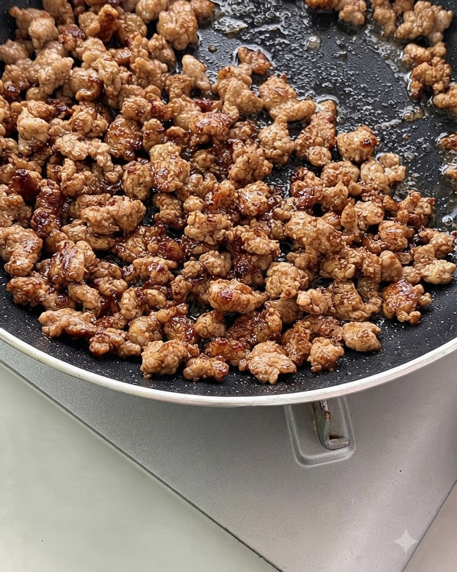 Carne macinata mescolata con cipollotti tritati e aglio sfrigolante in padella.