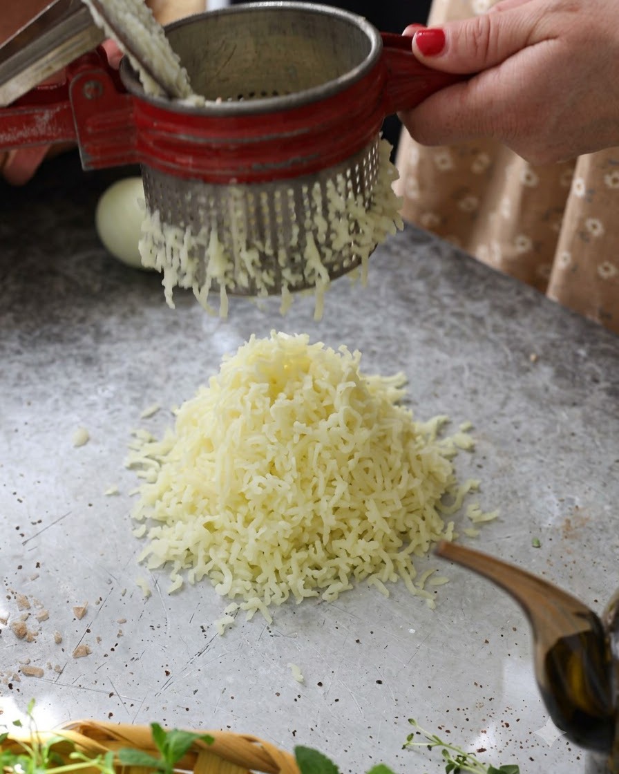 Patate lesse calde passate attraverso uno schiacciapatate rosso per formare un mucchio soffice sul tavolo.