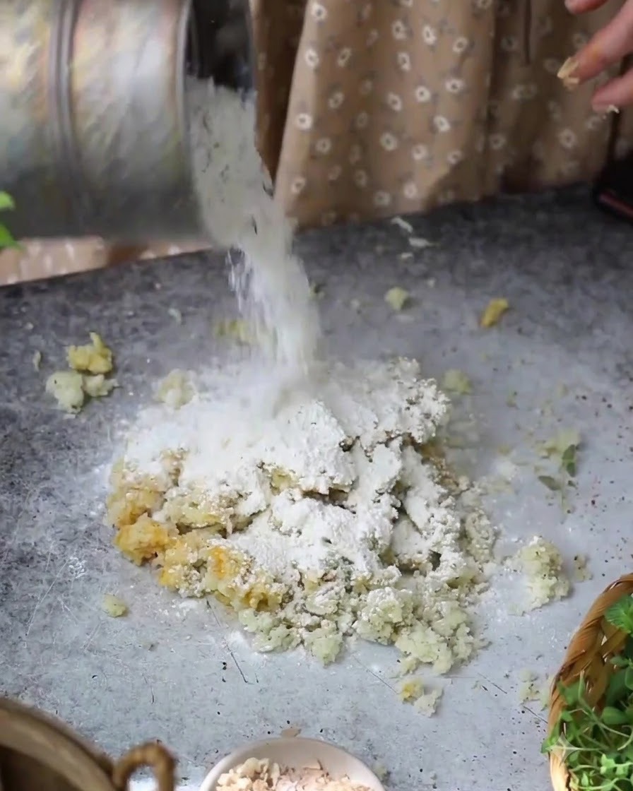 Farina versata da un contenitore sopra il composto di patate e uova sul tavolo.