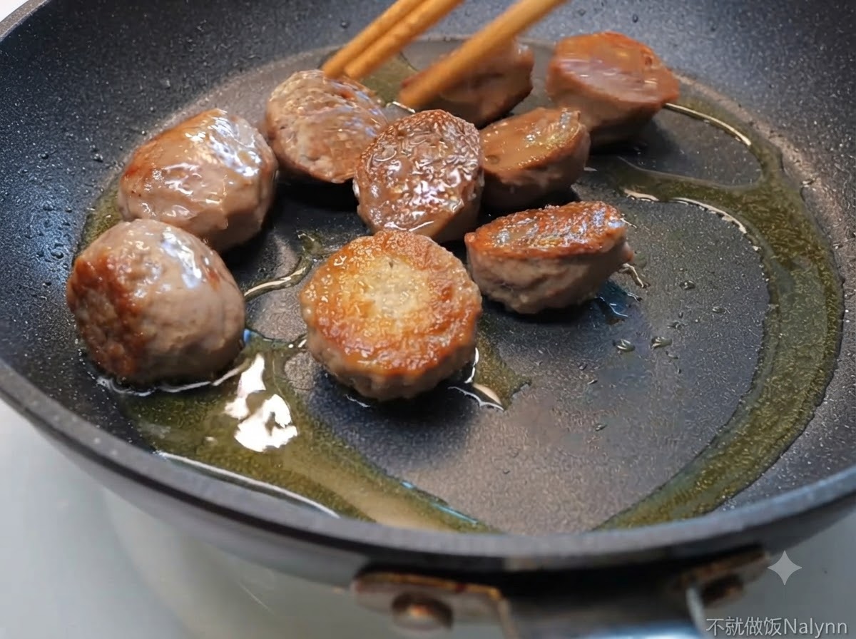 Metà di polpette di manzo che sfrigolano in una padella con olio, mosse da bacchette di legno.