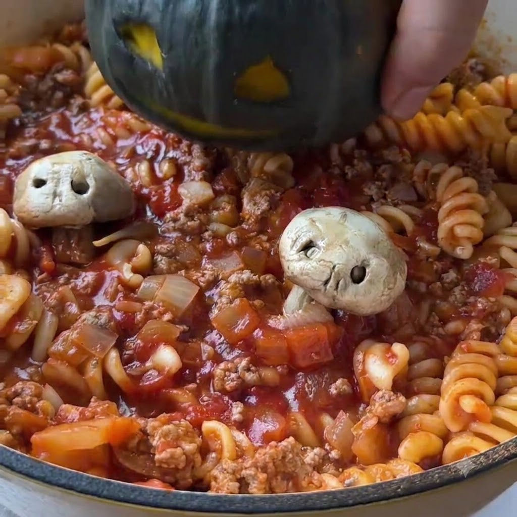 Una mini zucca verde scuro intagliata calata al centro di una padella riempita con pasta al pomodoro cotta e sugo di carne macinata.
