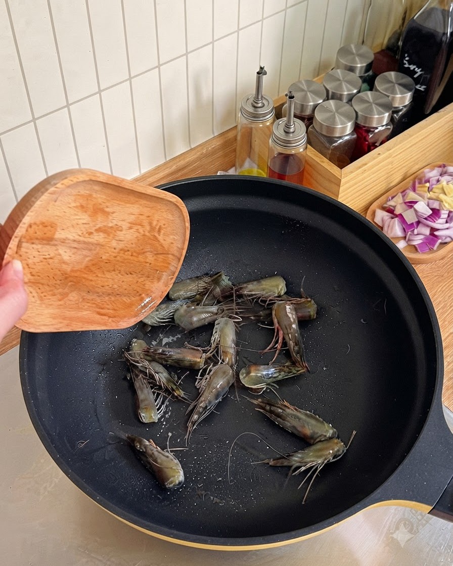 Teste di gamberi fritte e premute con una spatola di legno in un wok nero per ricavare lolio.