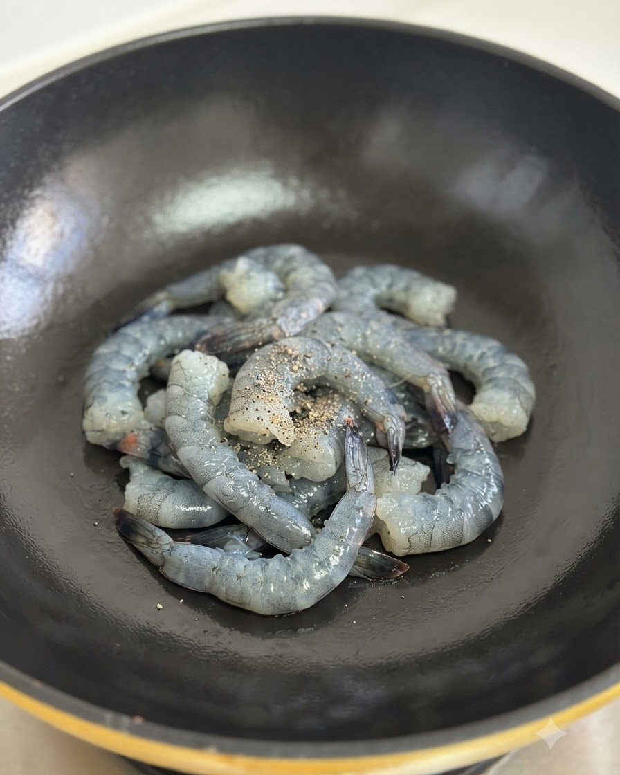 Gamberi crudi conditi con pepe nero in cottura allinterno di un wok nero.