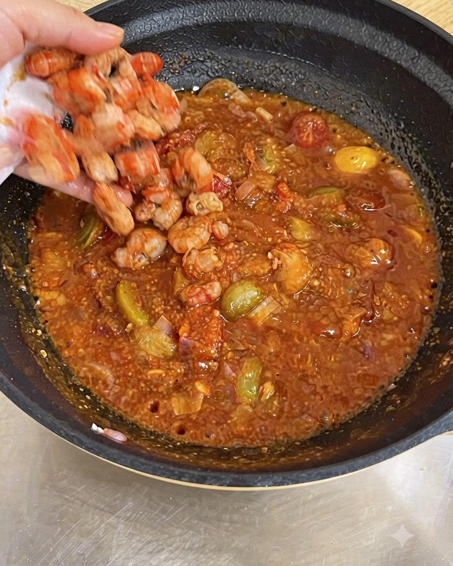 Una mano che lascia cadere i gamberi cotti in una padella piena di salsa di pomodoro rossa e bollente.
