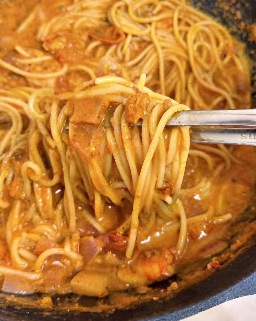 Pinze che sollevano fili di spaghetti ricoperti di salsa di pomodoro rosa e cremosa allinterno di un wok.