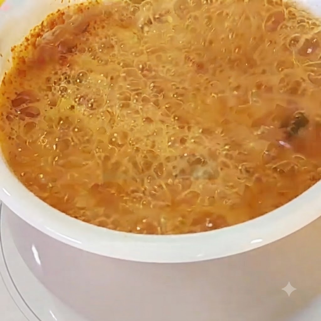 Un uovo rotto in una pentola di brodo di ramen rosso e bollente.