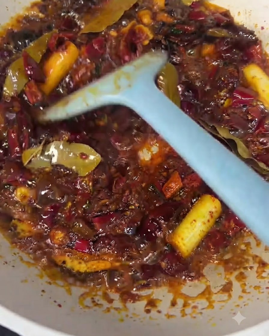 Pezzi di manzo mescolati nellolio al peperoncino rosso e nella base di spezie con una spatola blu.