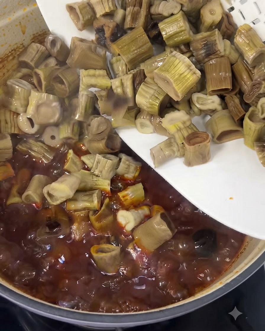Germogli di bambù tagliati che scivolano da un piatto bianco in uno stufato di manzo rosso che bolle.