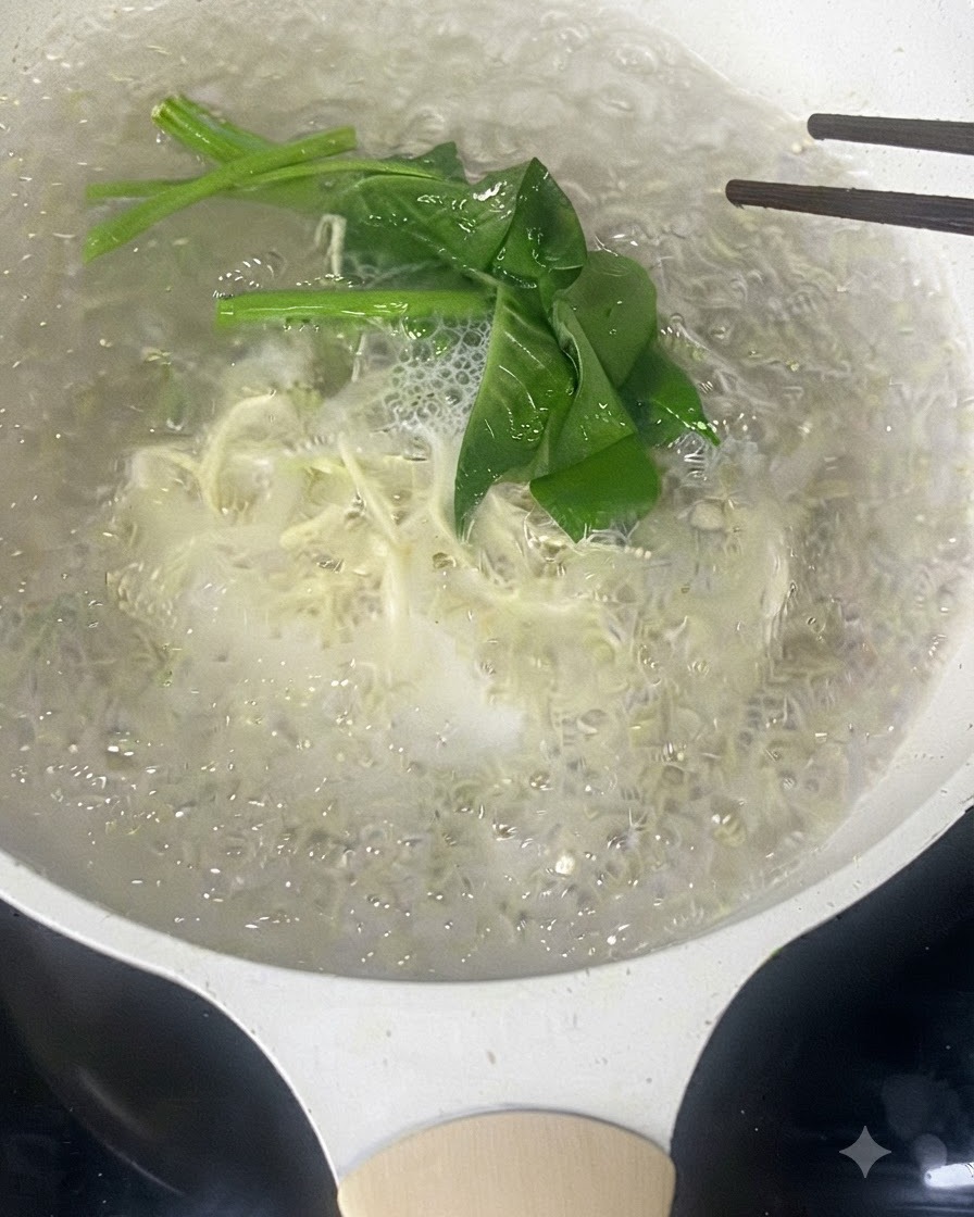 Bacchette che mescolano noodle bianchi sottili e verdure a foglia verde che bollono nellacqua.