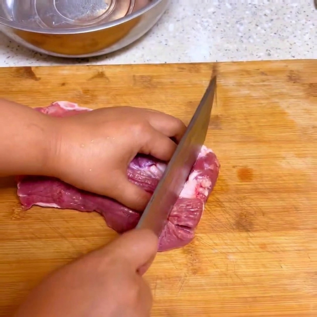 Un coltello da cucina che taglia manzo fresco crudo in grandi pezzi su un tagliere di legno.