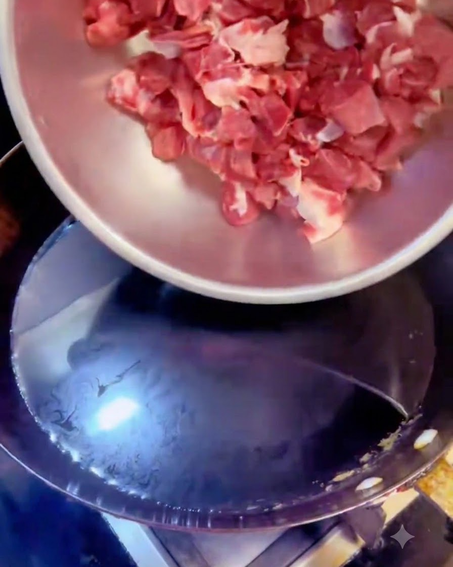 Cubetti di manzo versati da una ciotola dacciaio in una pentola di acqua bollente con aromi.