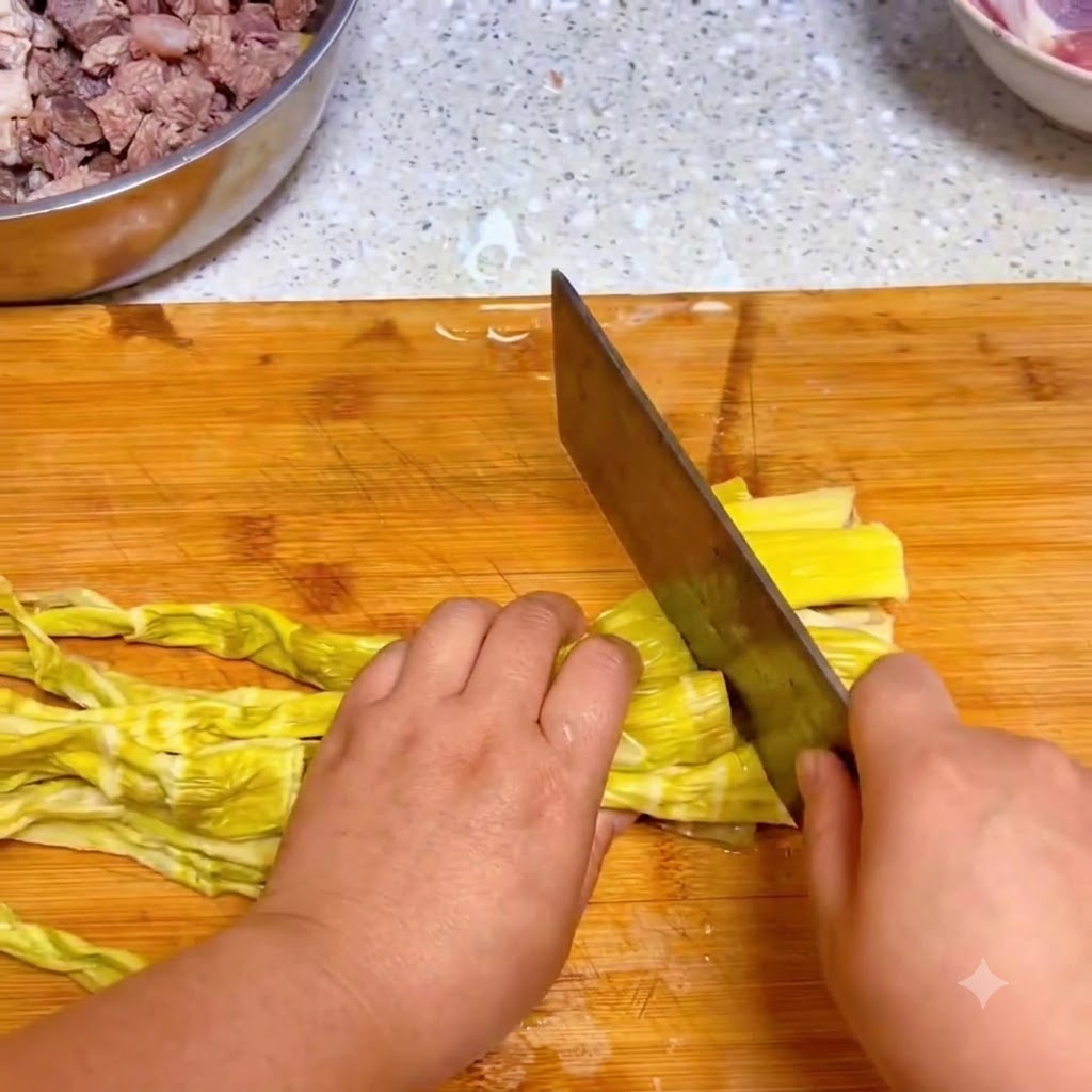 Un coltello da cucina che taglia germogli di bambù gialli reidratati su un tagliere di legno.