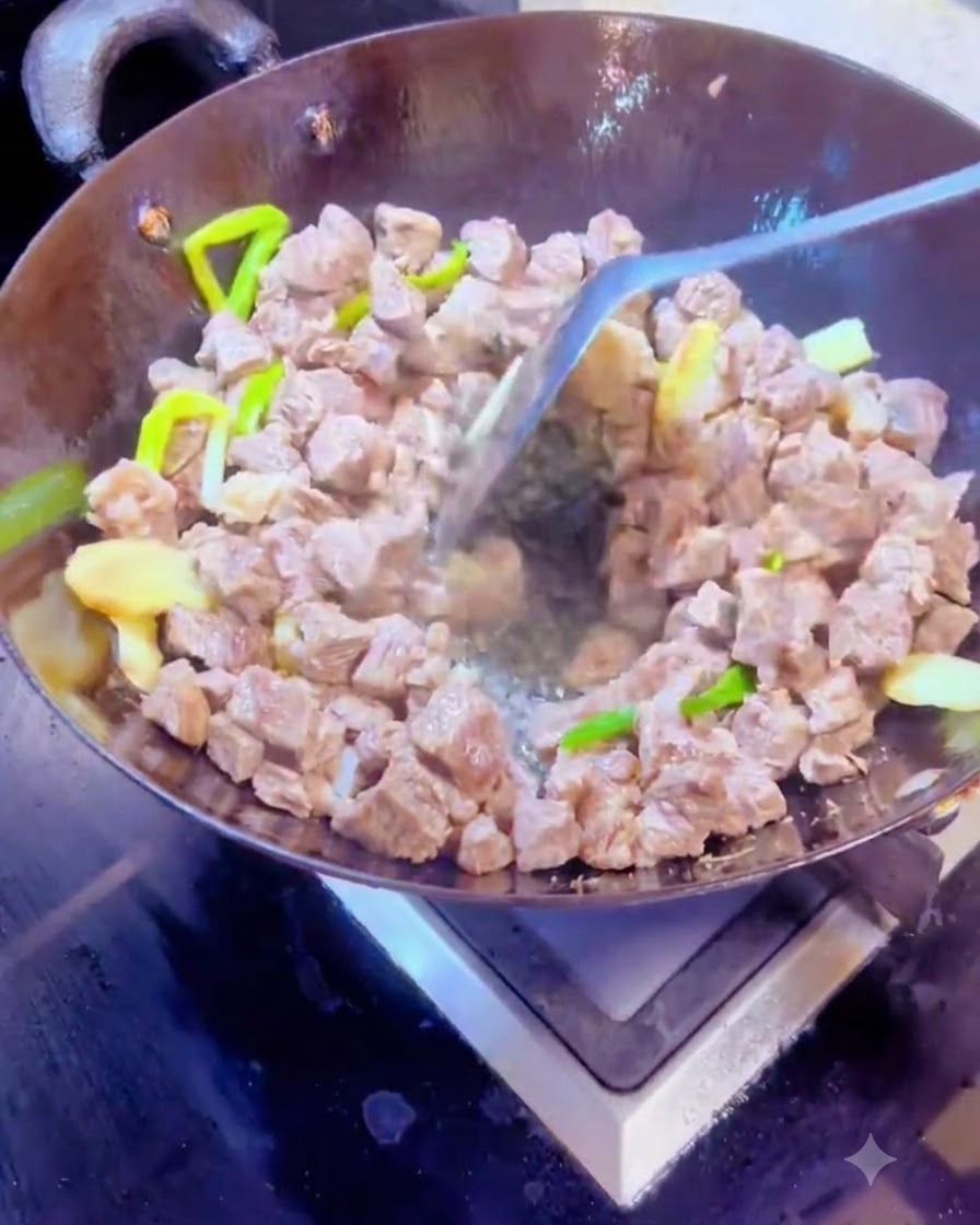 Mescolare spezie secche e cubetti di manzo insieme in un wok caldo usando una spatola di metallo.