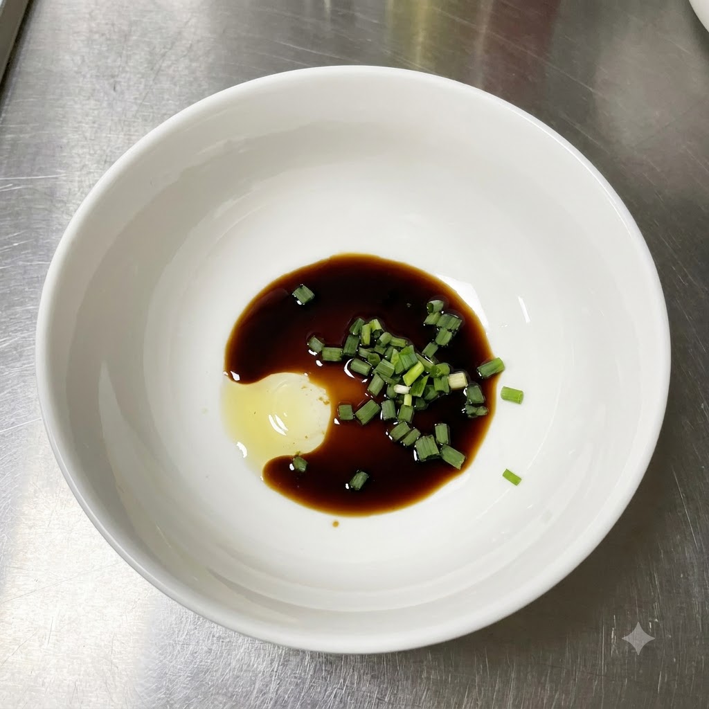 Una ciotola bianca contenente salsa di soia chiara, cipollotti verdi frescamente tritati e una cucchiaiata di pasta di condimento su un bancone in acciaio inossidabile.