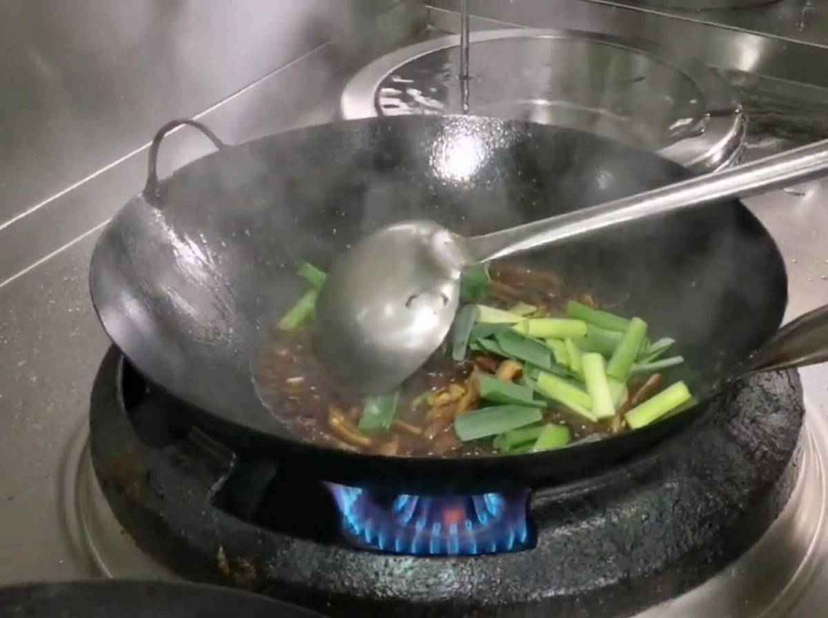 Sezioni di germogli daglio verde fresco aggiunte al wok e mescolate con gli ingredienti usando un mestolo.