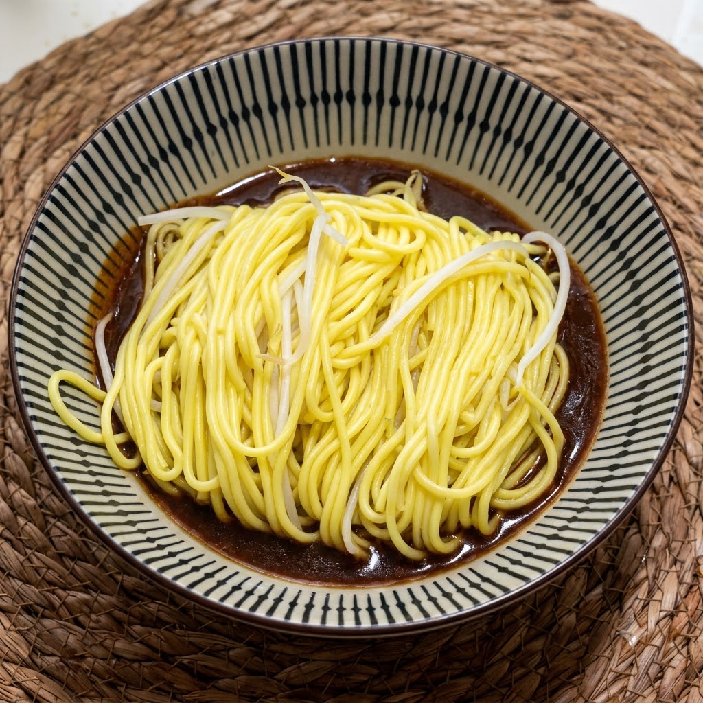 Una porzione di noodles gialli cotti e fumanti in una ciotola di ceramica decorata su una salsa ricca e scura.