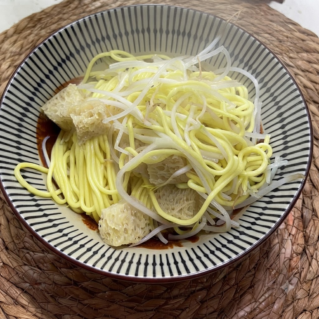 Noodles gialli cotti in una ciotola conditi con germogli di fagiolo mungo e verdure sottaceto croccanti.