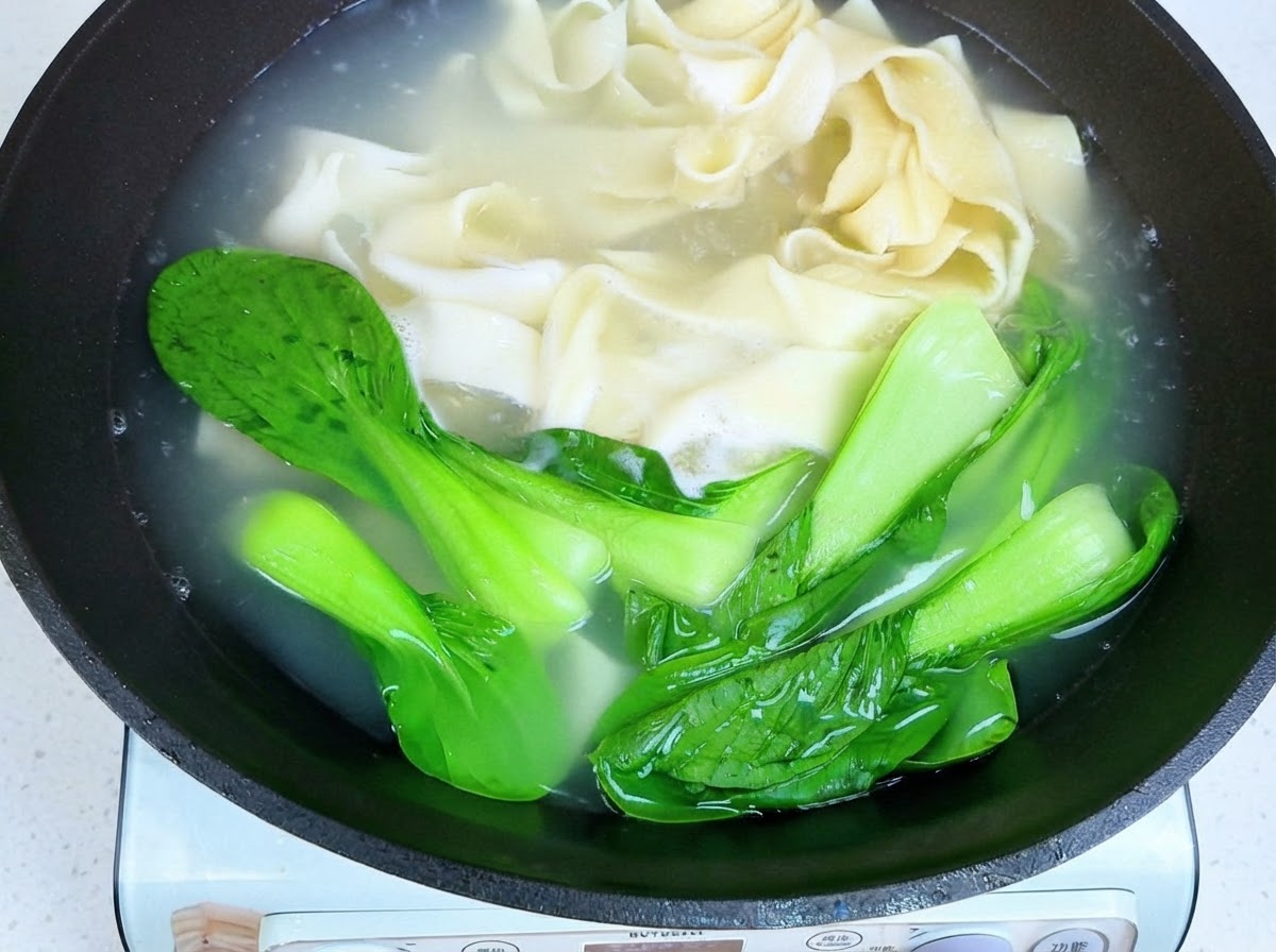 Bacchette che sollevano i noodles larghi cotti e il bok choy dallacqua calda.