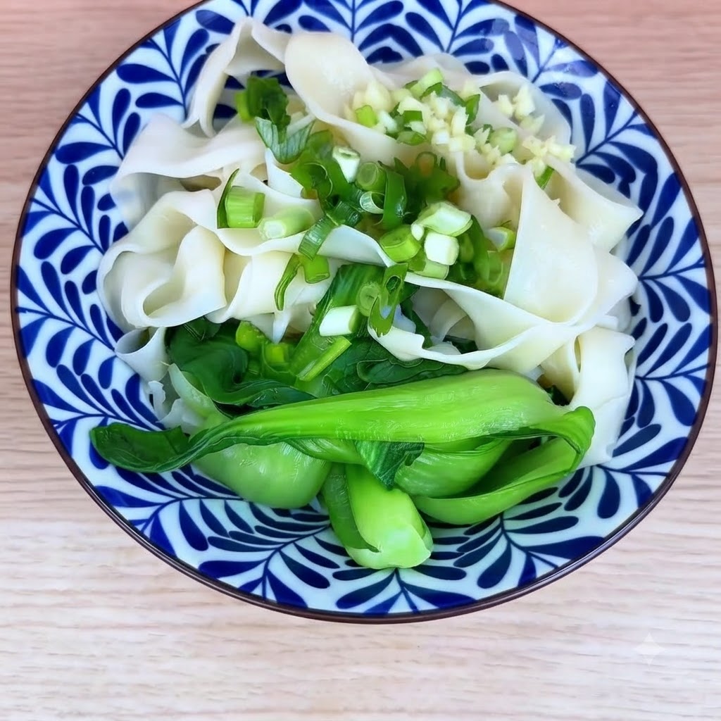 Una ciotola di noodles cotti e bok choy guarniti con cipollotti tritati e aglio tritato.