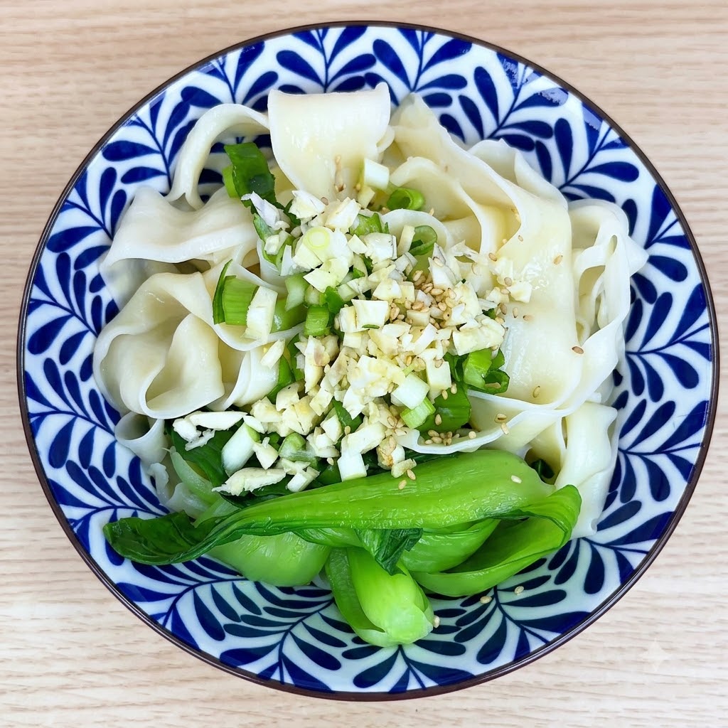 Semi di sesamo bianco e spezie cosparsi sopra laglio e i noodles in una ciotola.