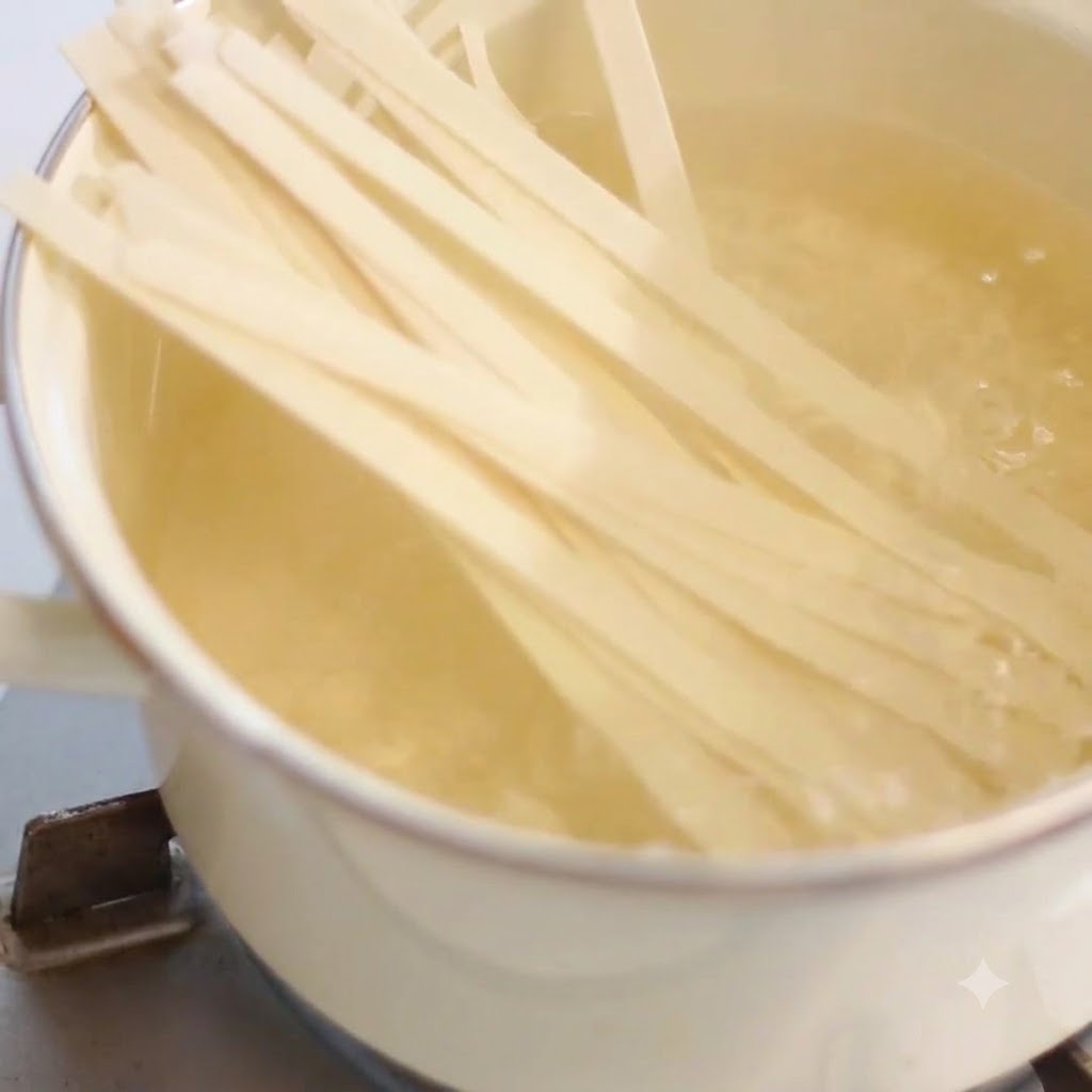 Noodles larghi in cottura dentro una pentola dacqua bollente su un piano cottura.