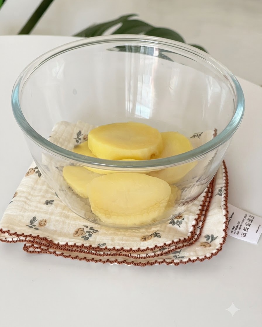 Fette di patate gialle cotte al vapore adagiate allinterno di una ciotola di vetro sopra un panno.