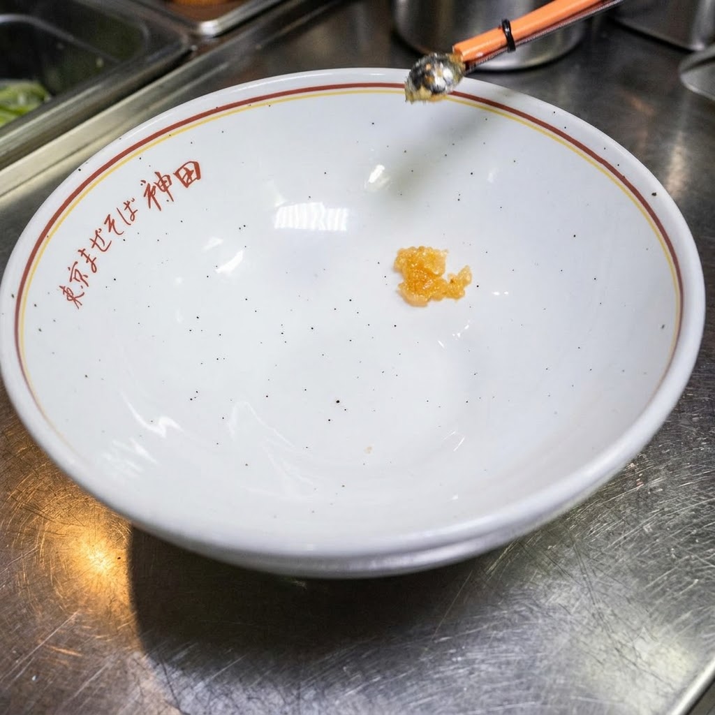 Una piccola quantità di liquido di condimento sul fondo di una ciotola bianca vuota con testo giapponese.